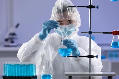 Scientist taking sample of light blue liquid in laboratory