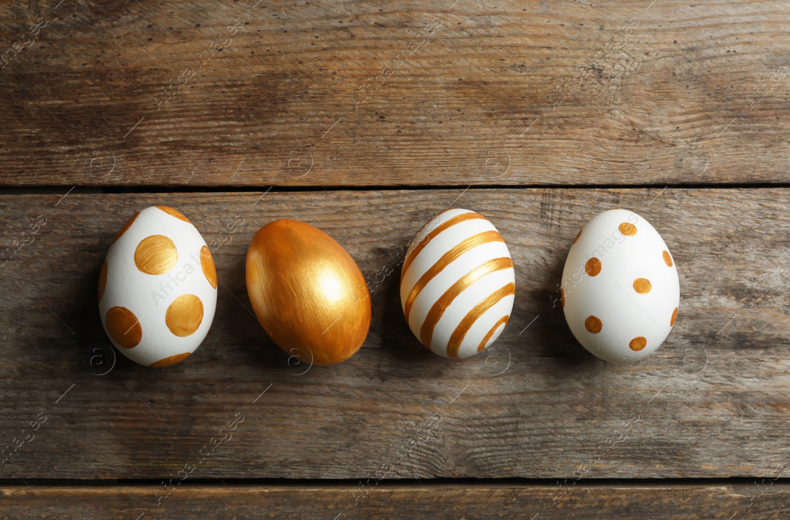 Photo of Set of traditional Easter eggs decorated with golden paint on wooden background, top view