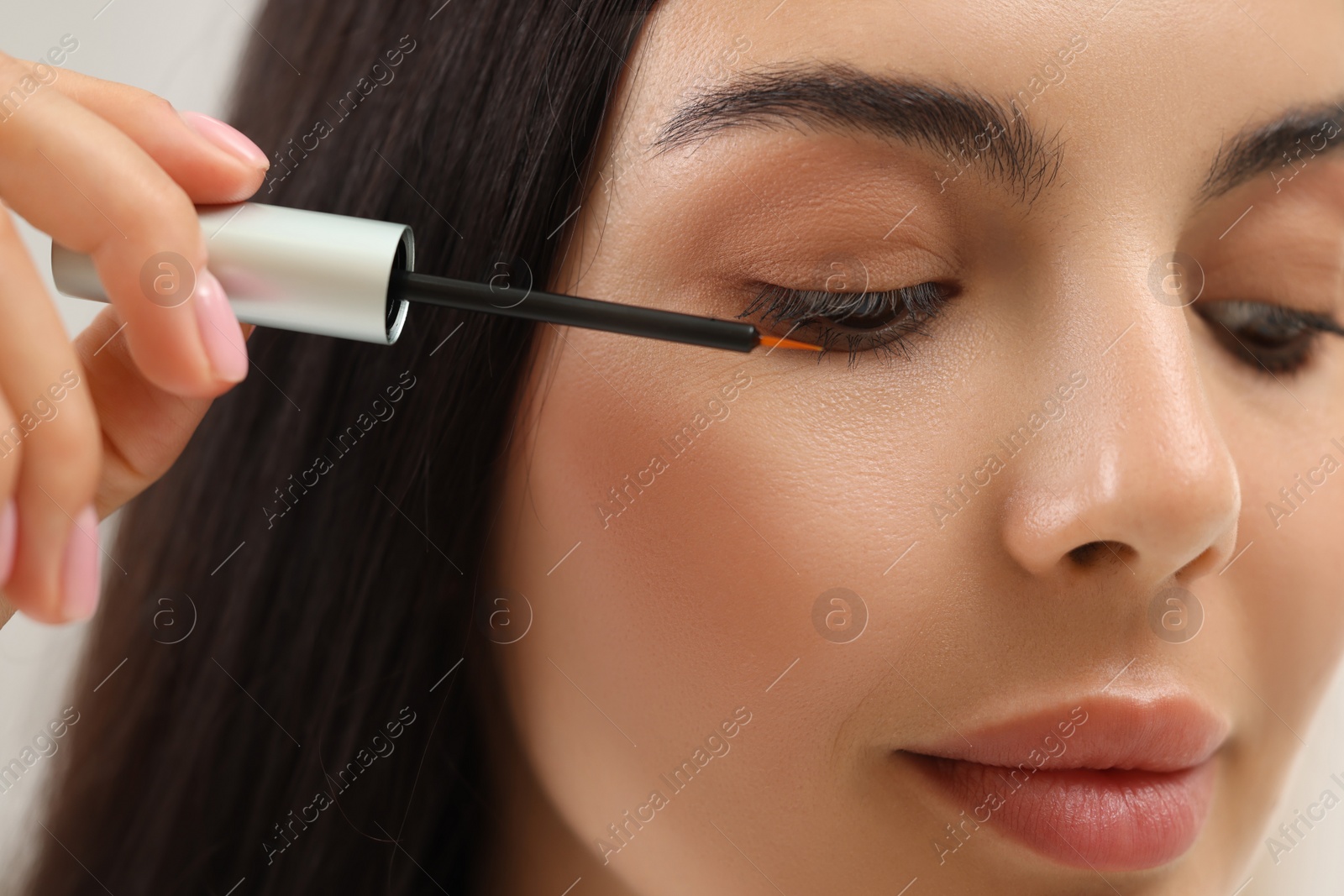 Photo of Beautiful woman applying serum onto her eyelashes, closeup. Cosmetic product