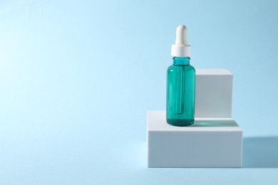 Presentation of bottle with cosmetic serum on light blue background, space for text