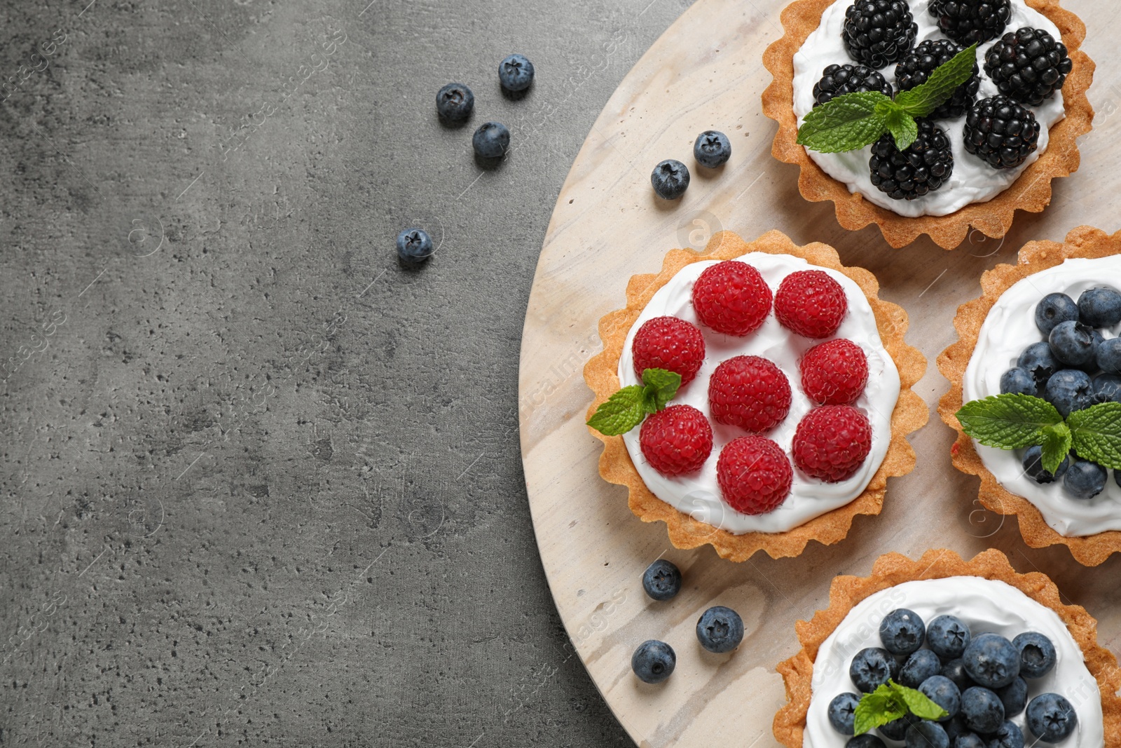 Photo of Tarts with different berries on grey table, top view with space for text. Delicious pastries