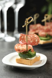 Photo of Tasty canapes with salami, cucumber and cream cheese on grey table