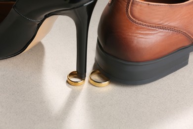 Photo of Woman's heel and man's shoe stepped on gold wedding rings against light gray background, closeup. Divorce concept