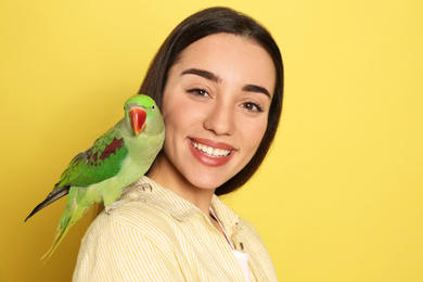 Young woman with Alexandrine parakeet on yellow background. Cute pet