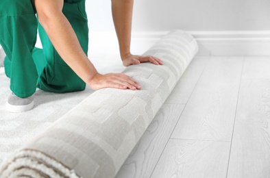 Man rolling out new carpet flooring indoors, closeup. Space for text