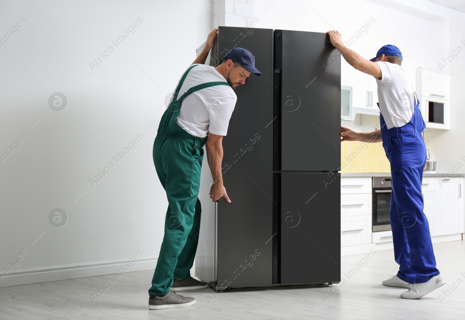 Photo of Professional workers carrying modern refrigerator in kitchen