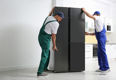 Photo of Professional workers carrying modern refrigerator in kitchen