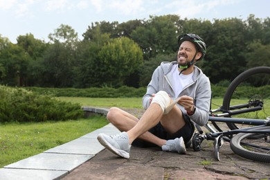 Photo of Man applying bandage onto his knee near bicycle outdoors, space for text