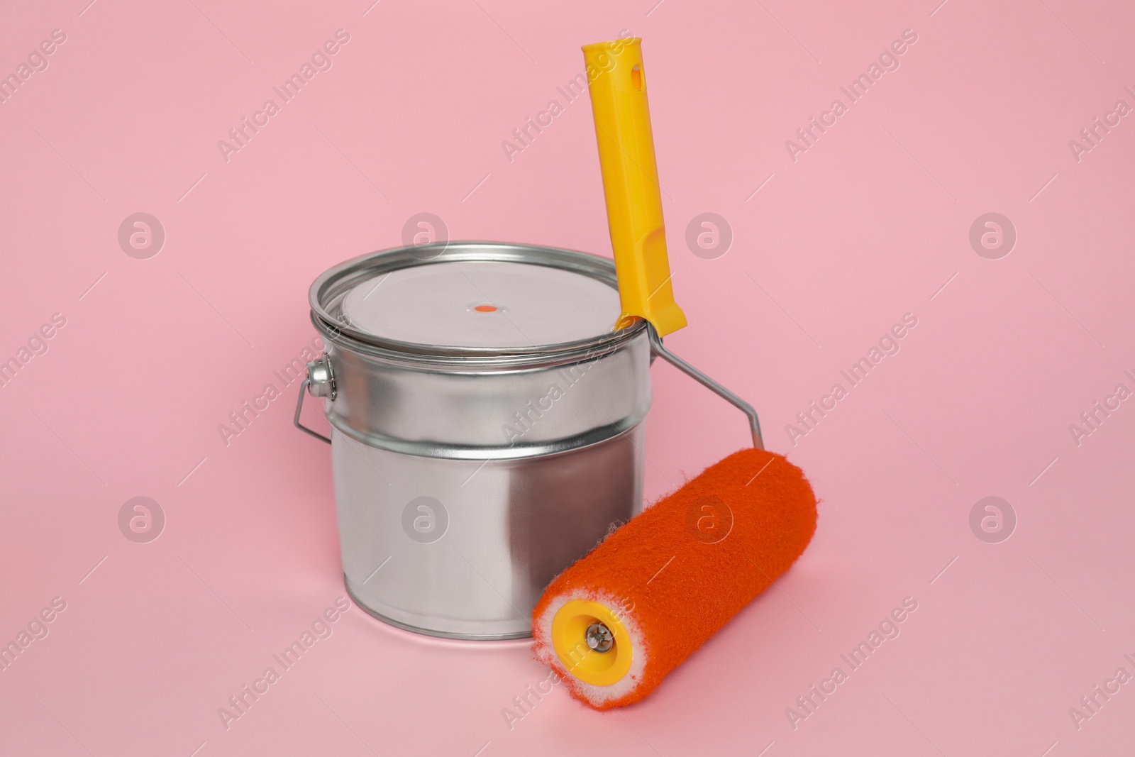 Photo of Can of orange paint and roller on pink background