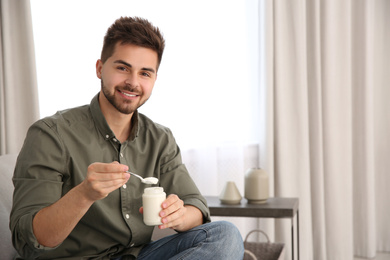Photo of Happy young man with tasty yogurt in living room. Space for text