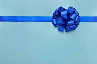 Photo of Ribbon with bow on light blue background, top view. Space for text