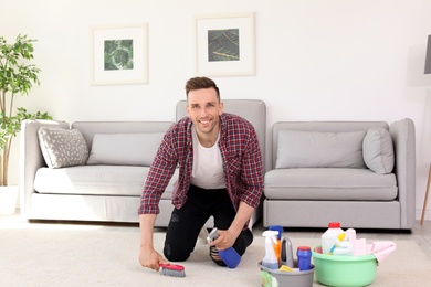 Photo of Young man cleaning carpet with brush at home