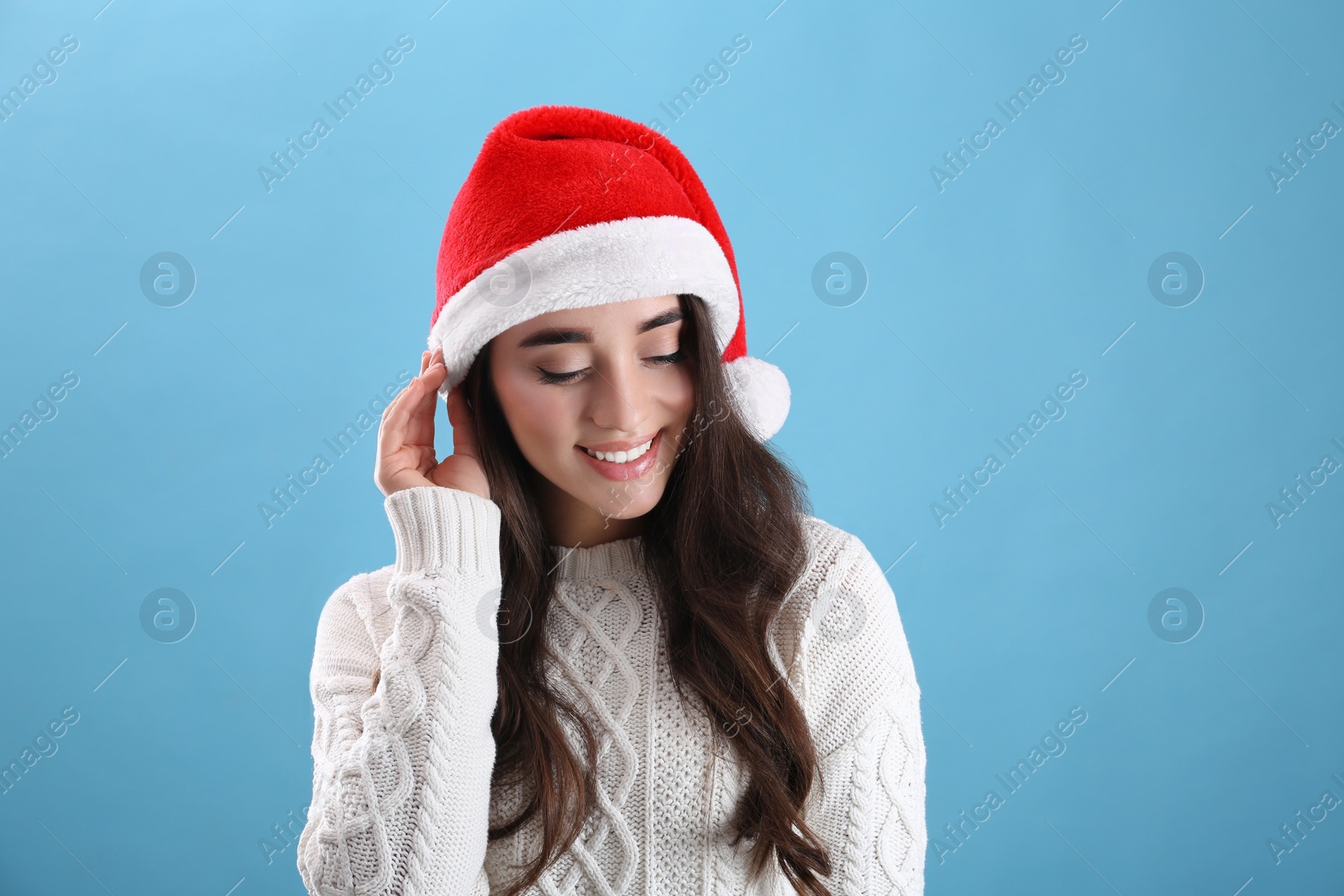 Photo of Beautiful woman wearing Santa Claus hat on light blue background