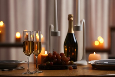 Photo of Glasses of champagne on wooden table against blurred burning candles
