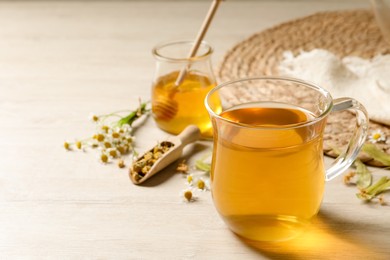 Photo of Freshly brewed tea and dried herbs on white wooden table. Space for text