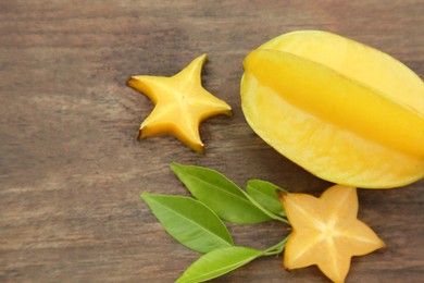 Photo of Cut and whole delicious ripe carambolas with leaves on wooden table