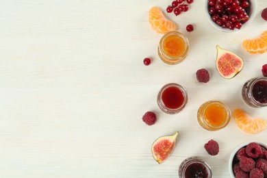 Flat lay composition with different sweet jams and ingredients on white wooden table. Space for text