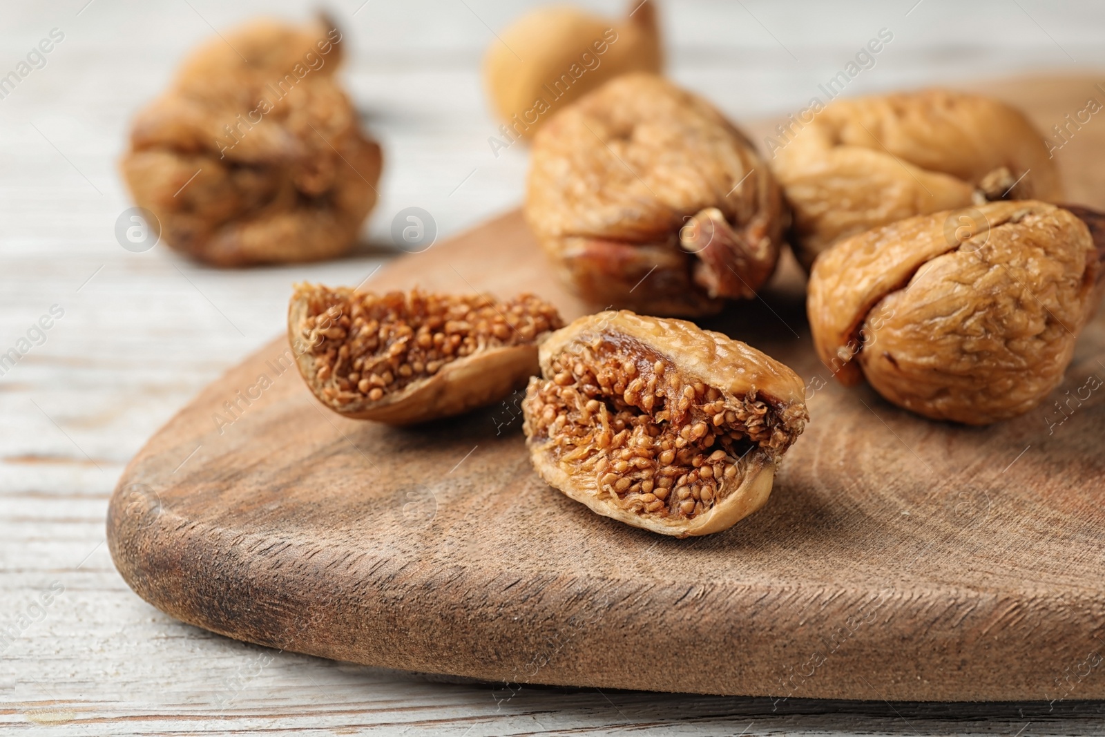 Photo of Wooden board with cut dried figs on white table, closeup