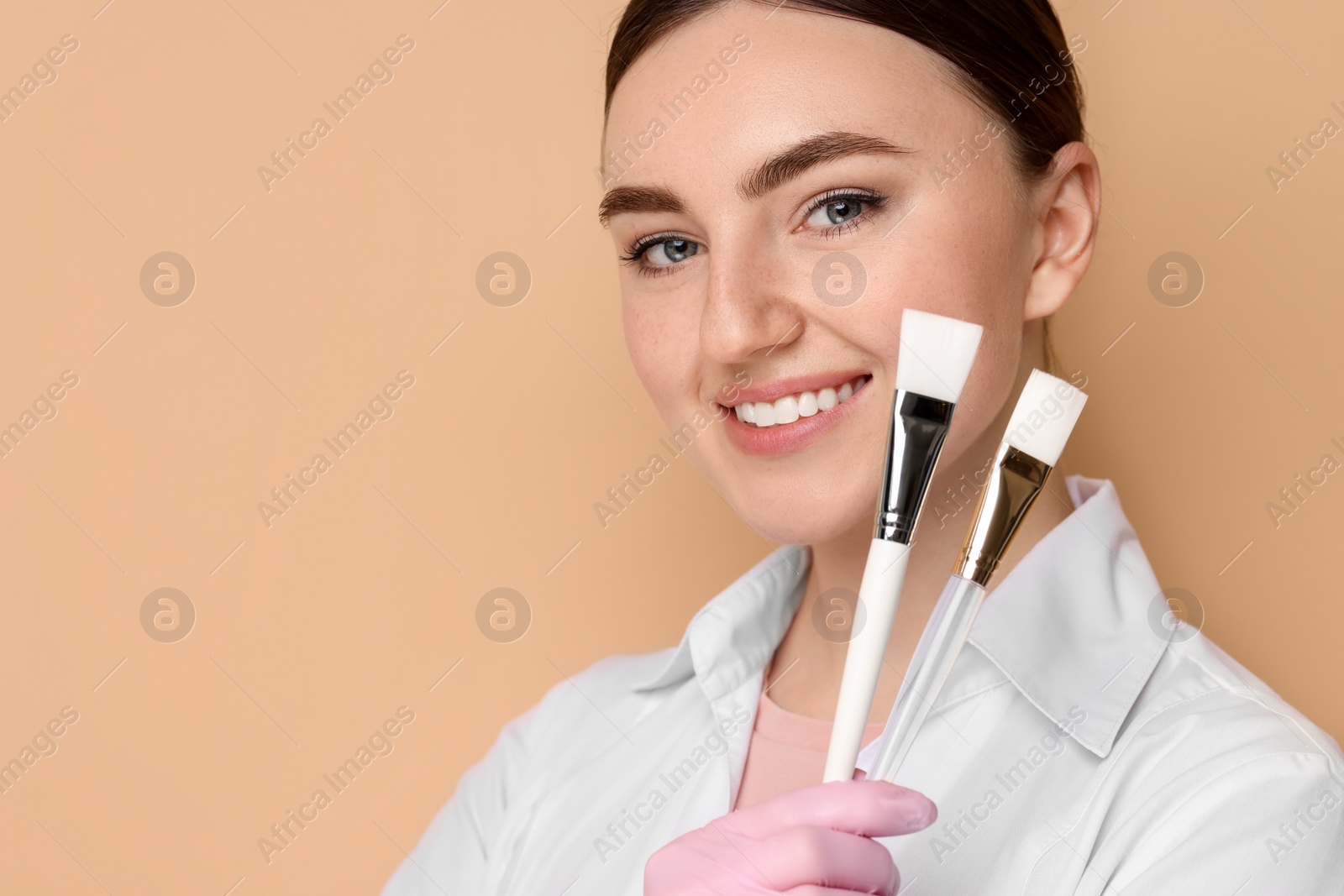 Photo of Cosmetologist with cosmetic brushes on beige background, space for text