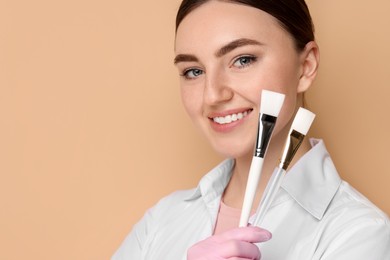 Cosmetologist with cosmetic brushes on beige background, space for text