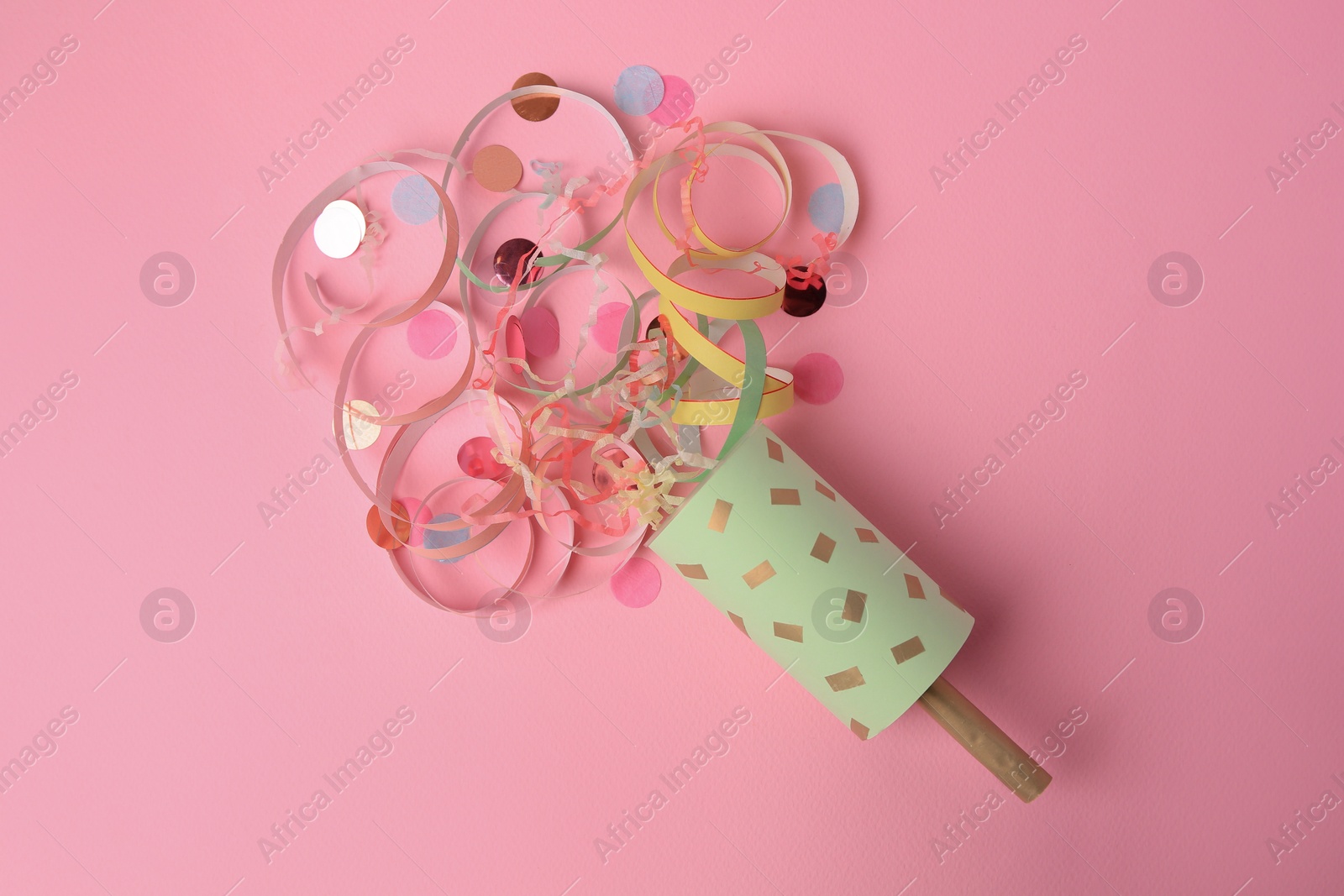 Photo of Beautiful serpentine and confetti bursting out of party popper on pink background, flat lay
