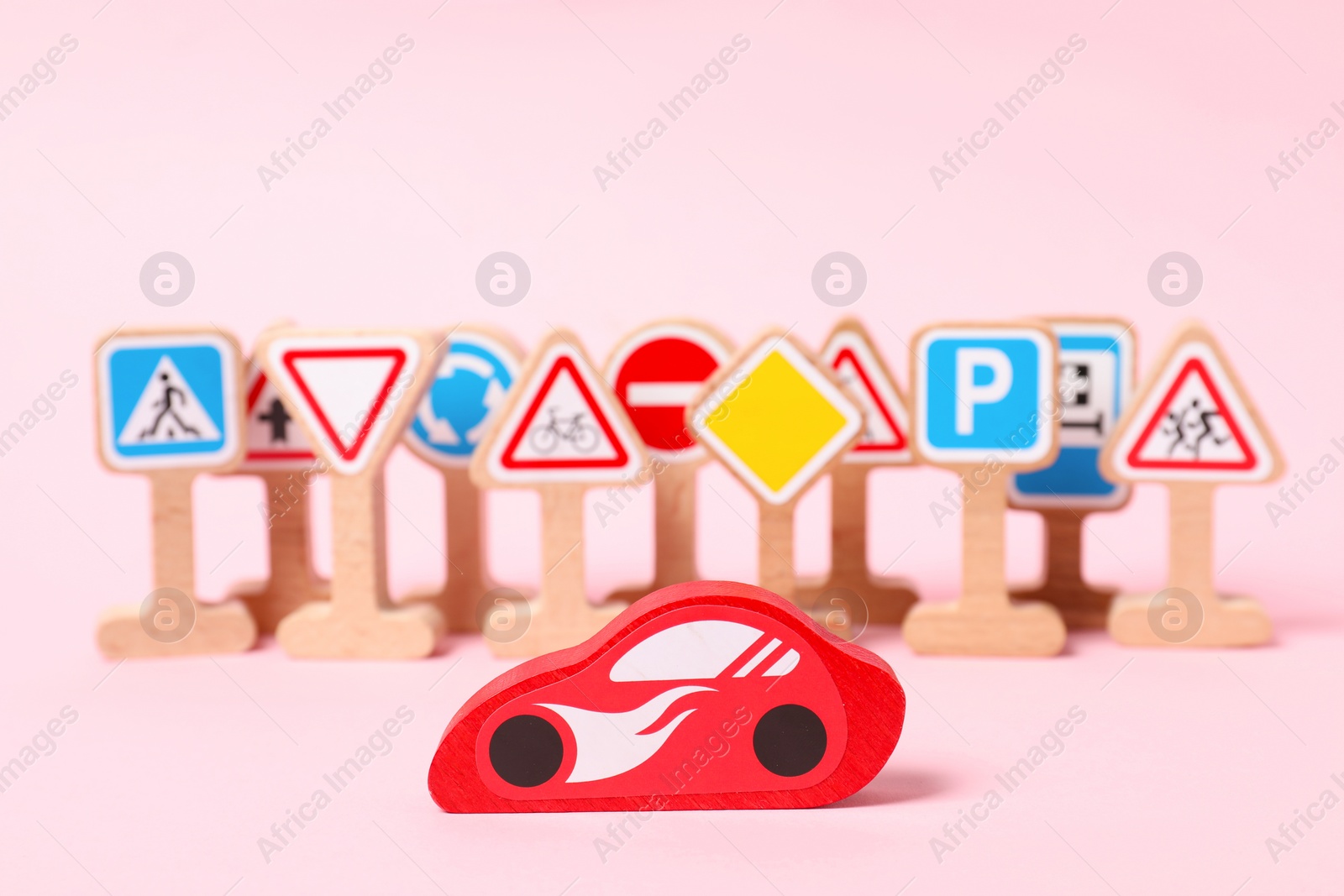 Photo of Set of wooden road signs and car on light pink background. Children's toy