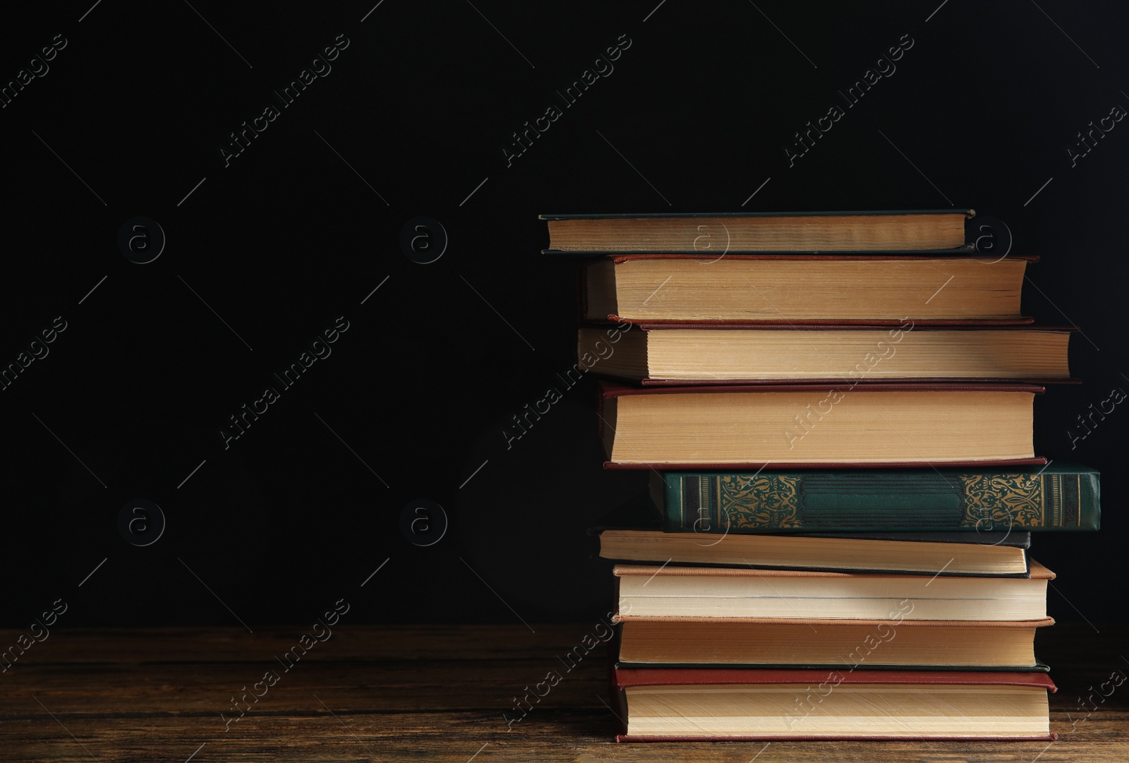 Photo of Collection of different books on wooden table against dark background. Space for text