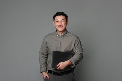 Portrait of happy businessman with laptop on grey background