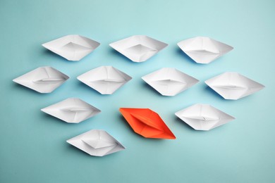 Photo of Orange paper boat floating away from others on light background, flat lay. Uniqueness concept