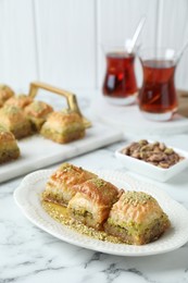 Photo of Delicious fresh baklava with chopped nuts and honey on white marble table. Eastern sweets