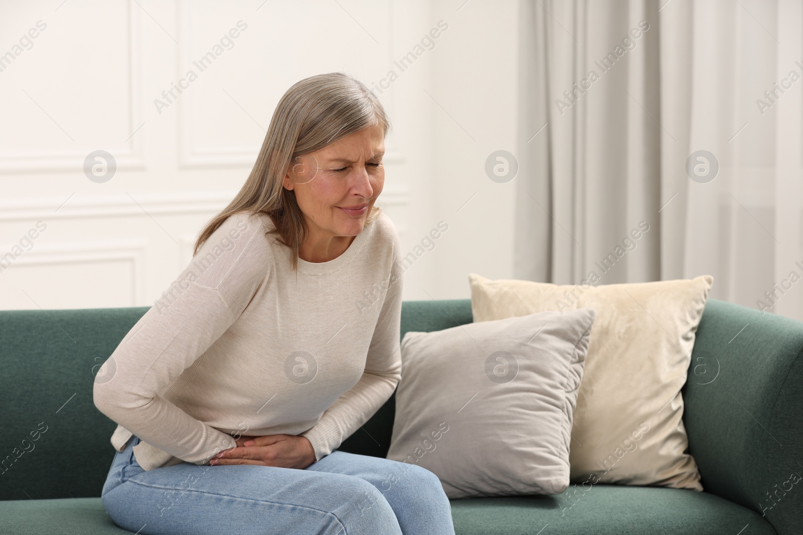 Photo of Menopause. Woman suffering from abdominal pain on sofa at home