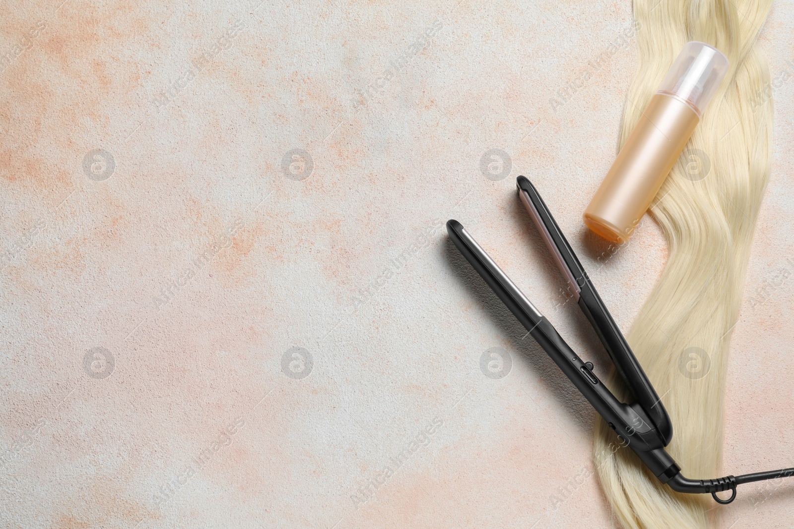 Photo of Spray bottle with thermal protection, lock of blonde hair and modern straightener on beige textured table, flat lay. Space for text