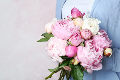 Woman with bouquet of beautiful peonies on pink background, closeup