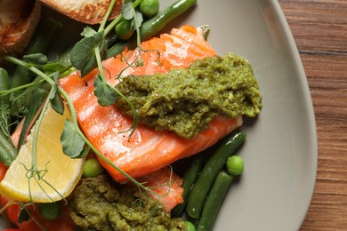 Photo of Tasty cooked salmon with pesto sauce served on wooden table, closeup