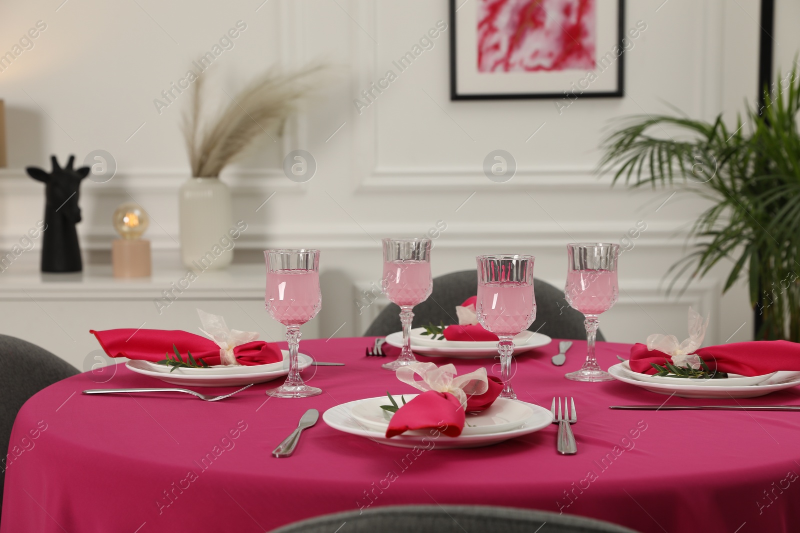 Photo of Color accent table setting. Glasses, plates, cutlery and pink napkins on table indoors