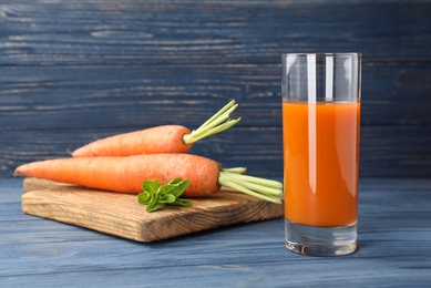 Photo of Glass of drink and carrots on wooden table, space for text