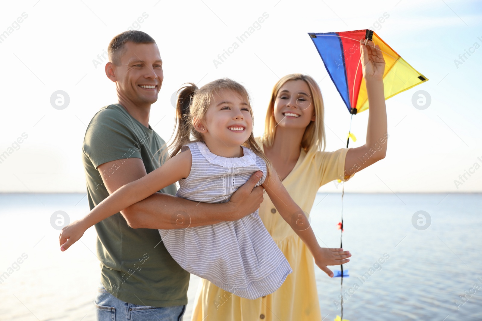 Photo of Happy parents with their child playing with kite on beach. Spending time in nature