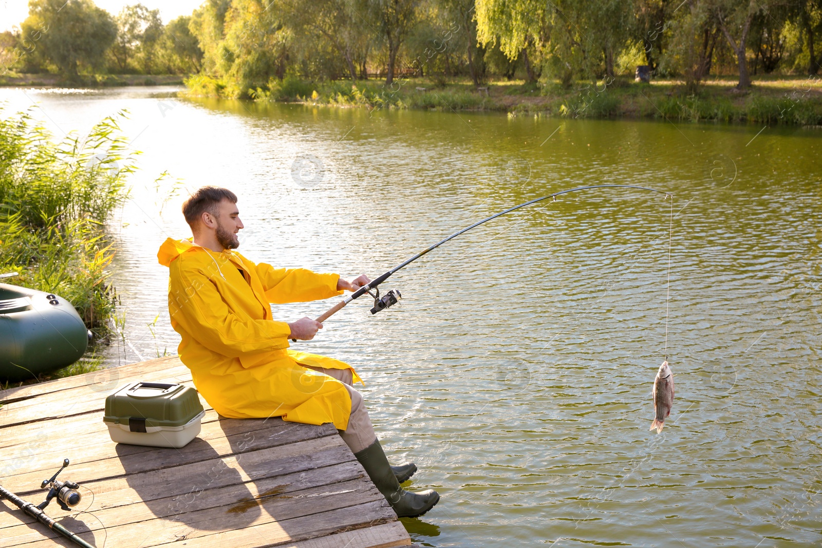 Photo of Man with rod fishing on wooden pier at riverside. Recreational activity