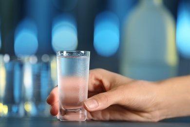 Woman with shot of vodka at table in bar, closeup