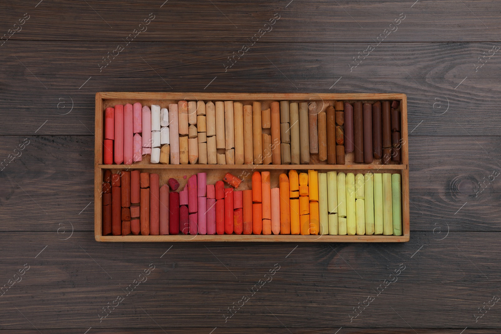 Photo of Drawing pastel set in box on wooden background, top view