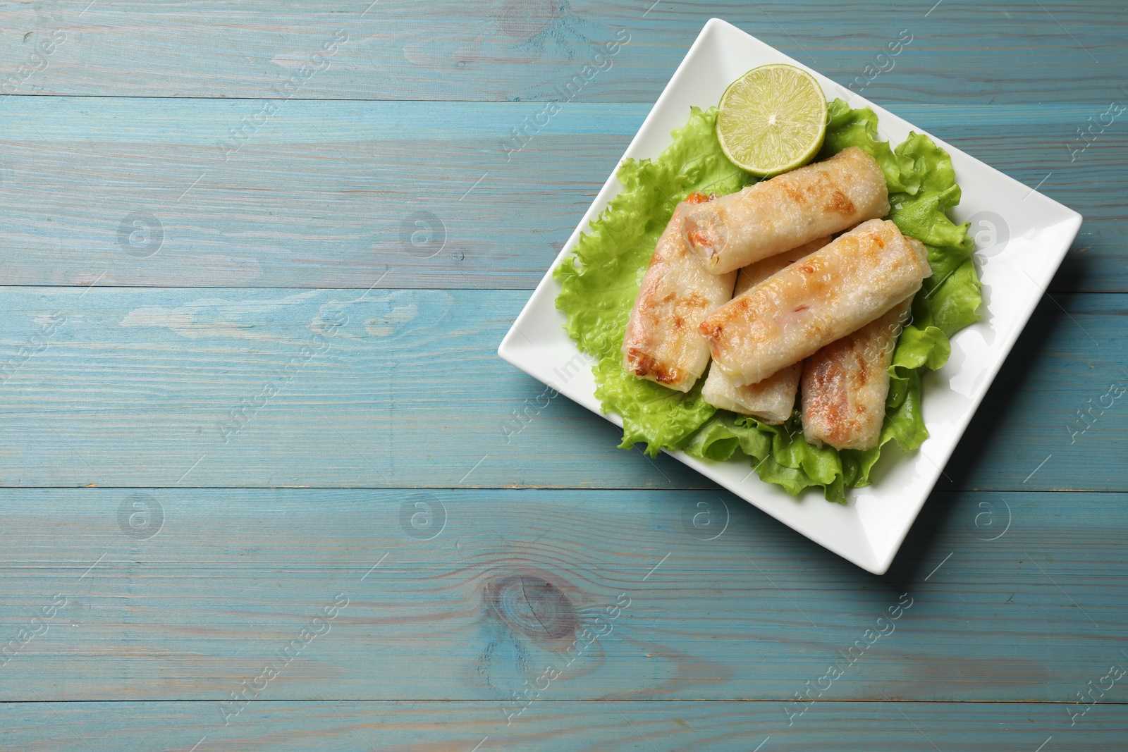 Photo of Delicious fried spring rolls on light blue wooden table, top view. Space for text