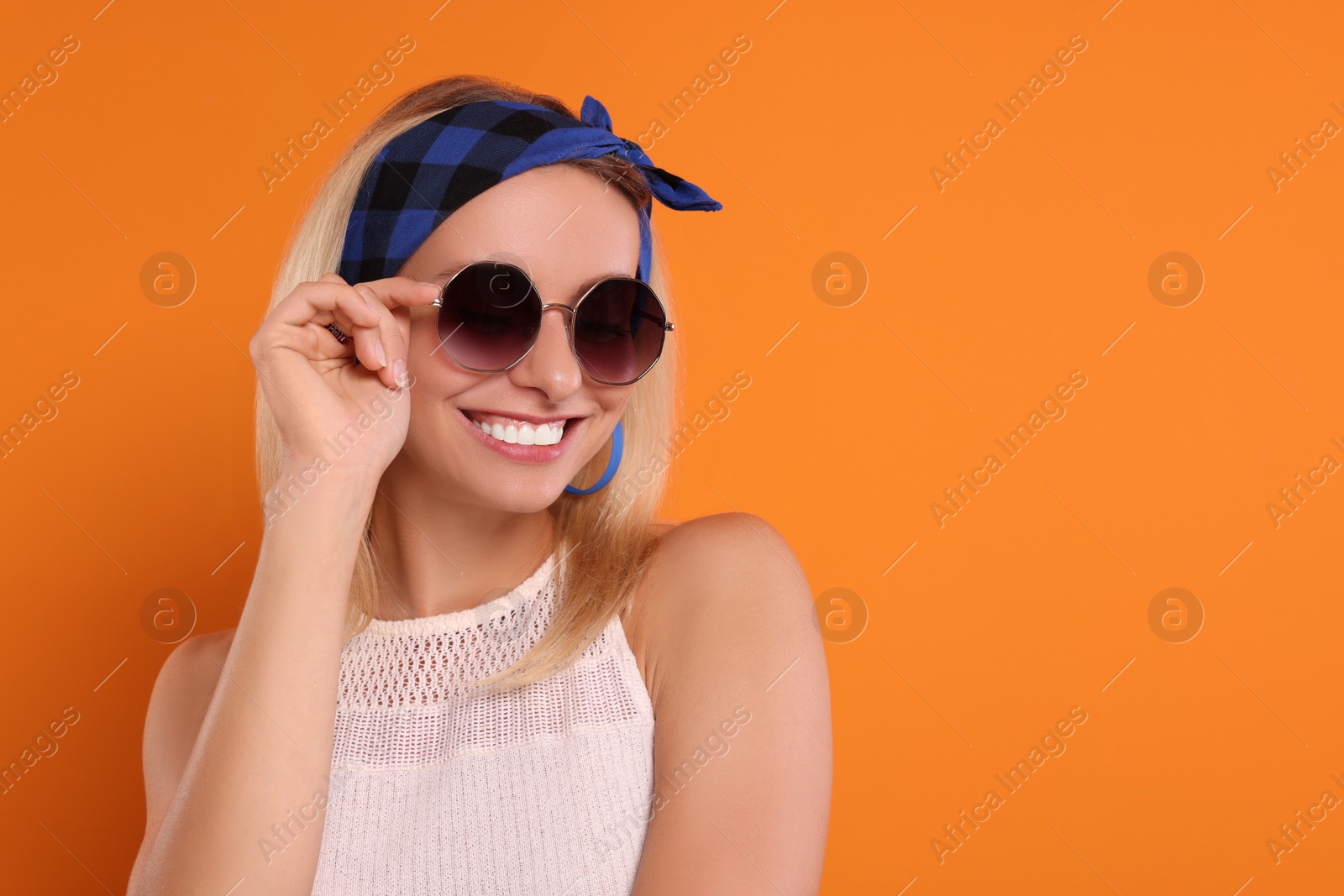 Photo of Portrait of smiling hippie woman in sunglasses on orange background. Space for text