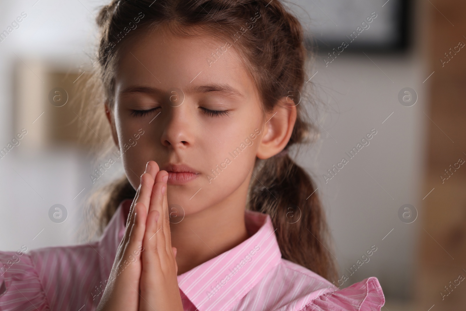 Photo of Cute little girl with hands clasped together praying at home