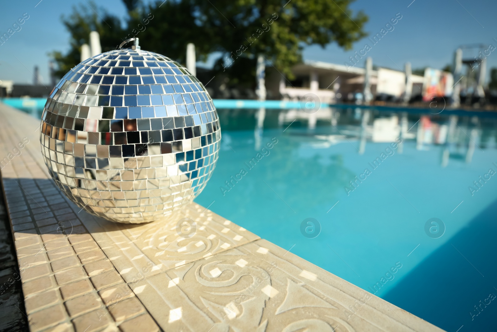 Photo of Shiny disco ball on edge of swimming pool. Party decor