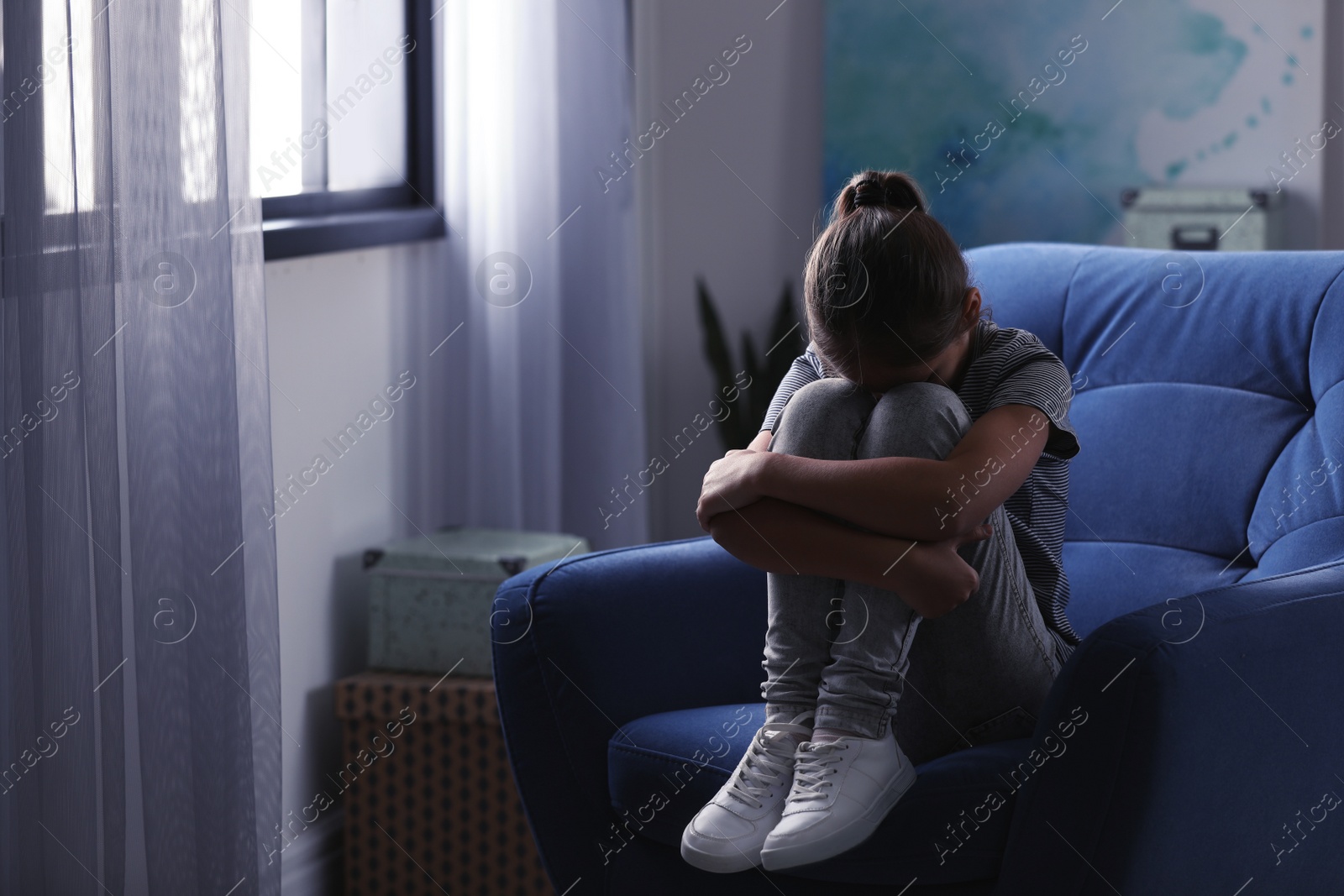 Photo of Depressed preteen girl sitting in armchair at home