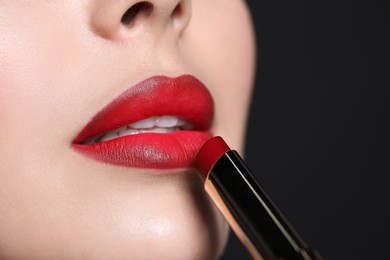 Photo of Young woman applying red lipstick on black background, closeup