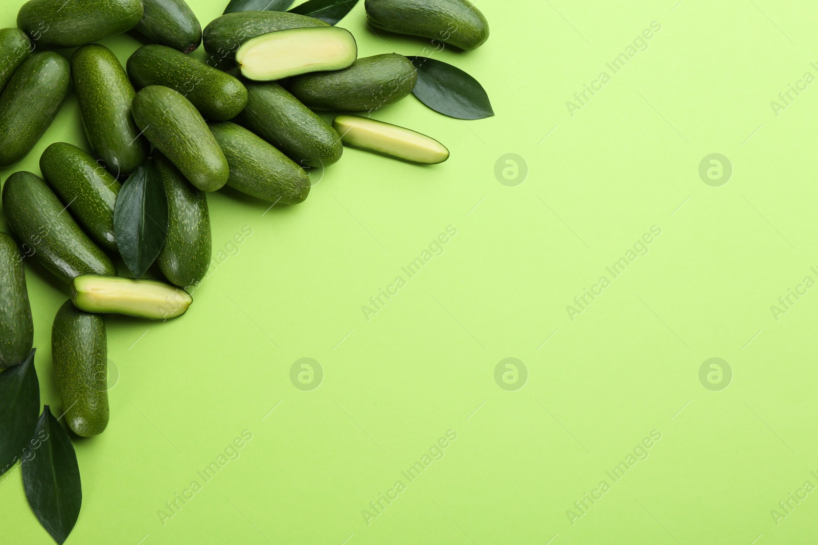 Photo of Whole and cut seedless avocados with leaves on green background, flat lay. Space for text
