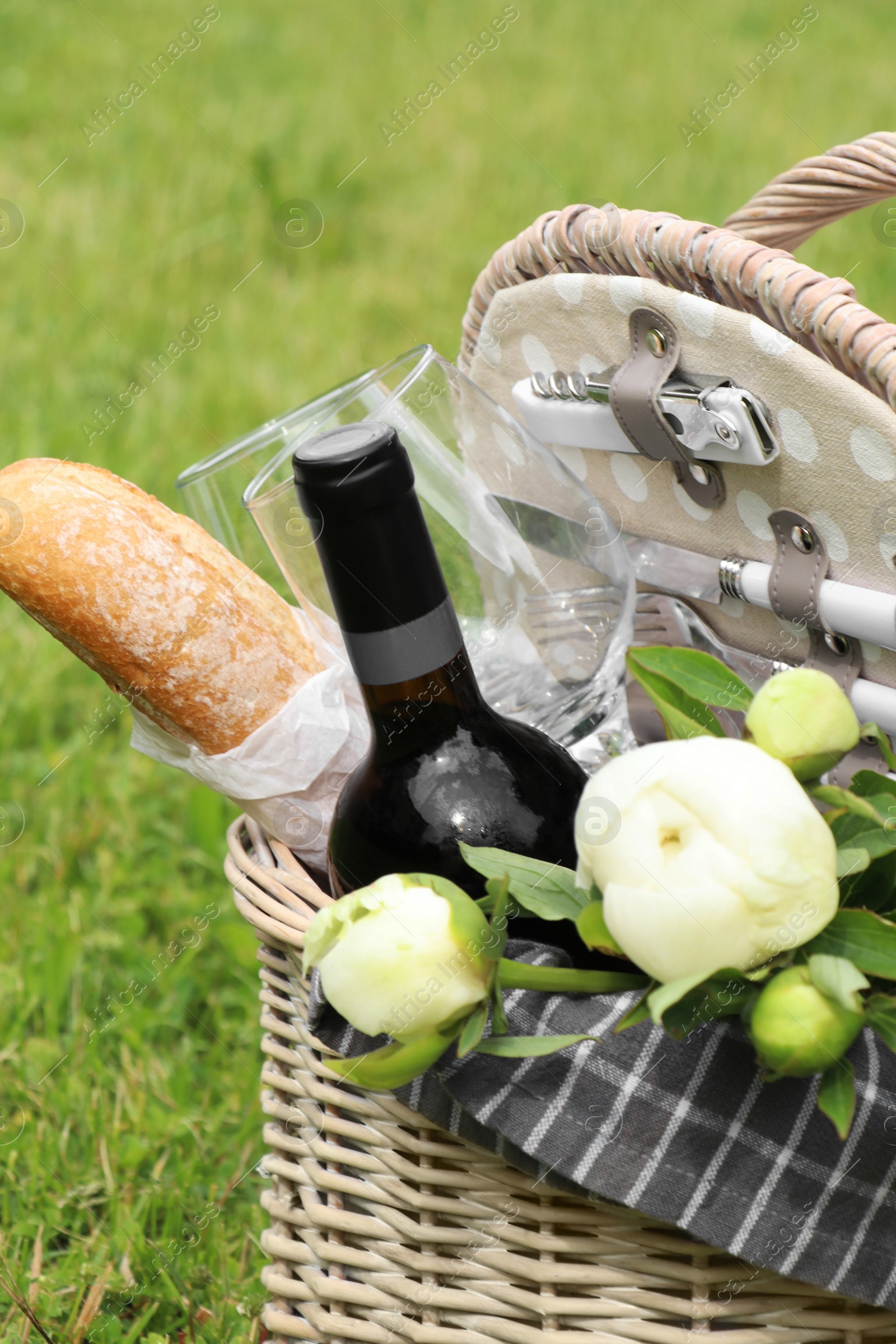 Photo of Picnic basket with wine, bread and flowers on green grass outdoors