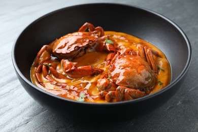 Photo of Delicious boiled crabs with sauce in bowl on grey textured table, closeup