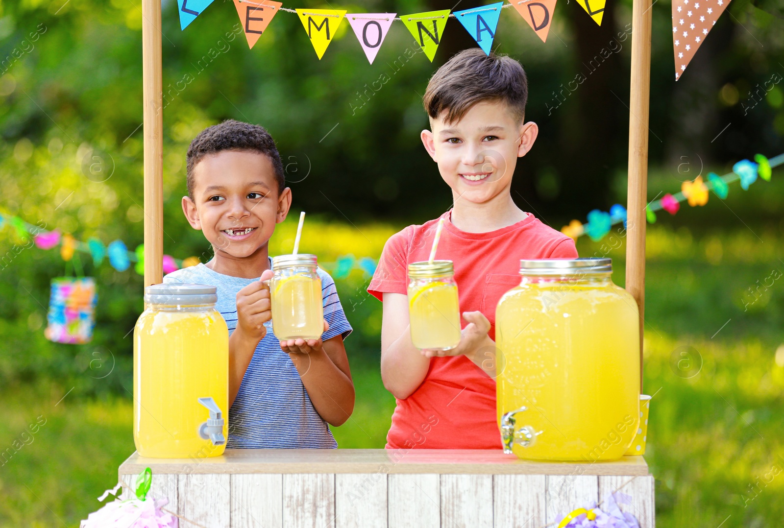 Photo of Cute little boys at lemonade stand in park. Summer refreshing natural drink